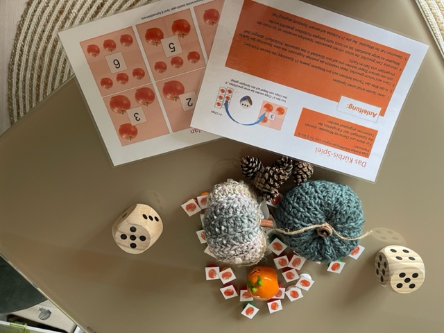 2 gehäkelte Kürbisse, verschiedene kleine Spielkarten mit Kürbismotiv 2 größere Würfel, die Anleitung und eine Frosch Figur