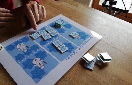 ein/-e Klient/-in mit dem Schneegestöber Spielplan und eine Reihe an Spielplaketten mit einer Schneeflocke