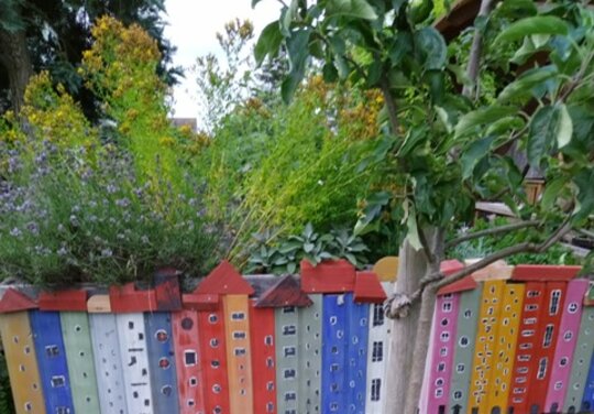ein kleiner Garten mit einer Aneinanderreiung von bunten Holzpfählen, gestaltet als Häuser