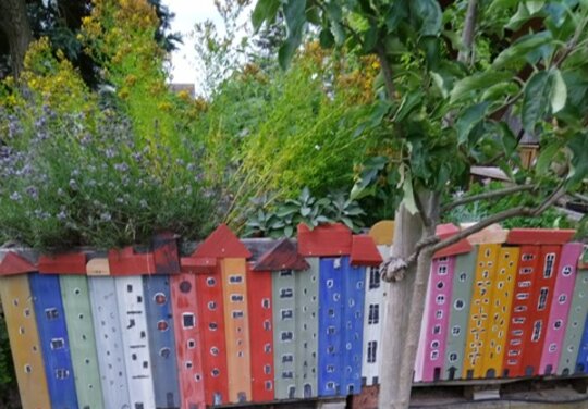 ein kleiner Garten mit einer Aneinanderreiung von bunten Holzpfählen, gestaltet als Häuser
