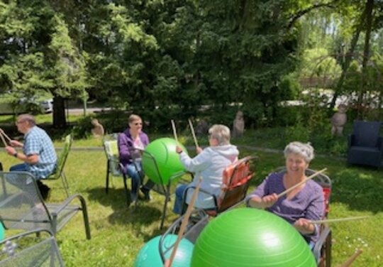 mehrere Personen Trommeln in einem Garten auf Gymnastikbällen