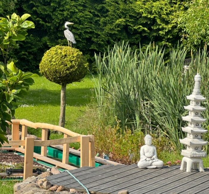 Kneipp-Gelände im Grünen Kneipp-Gelände - von Bäumen umgeben, rechts eine weiße Buddha-Statue und ein Turm, auf einem kleinen Baum ein Storch