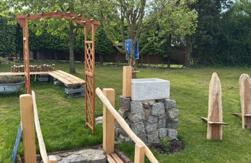 ein Garten mit einem hölzernern Torbogen, einer Stizbank und einem Steinbecken