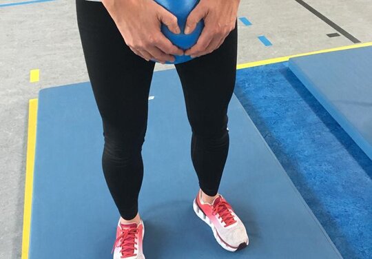 eine Person hält einen kleinen Gymnastikball unterhalb des Bauches