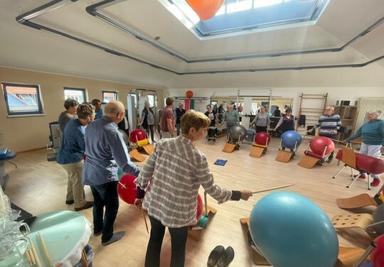 eine große Gruppe Menschen die mit Trommelstöckern auf Gymnastikbälle trommeln