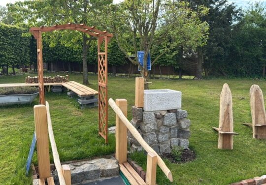 ein Garten mit einem hölzernern Torbogen, einer Stizbank und einem Steinbecken