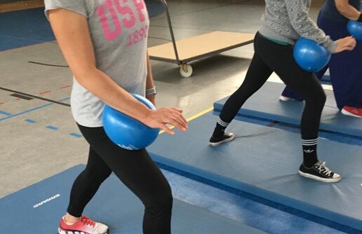 Funktionstraining, mehrere Personen klemmen Ball zwischen Unterarm und Oberschenkel