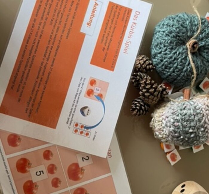 2 gehäkelte Kürbisse, verschiedene kleine Spielkarten mit Kürbismotiv 2 größere Würfel, die Anleitung und eine Frosch Figur