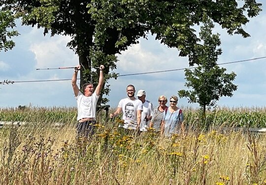 fünf Personen draussen in der Natur mit Gehstöckern, die Person links hebt seine Stöcker mit Freude